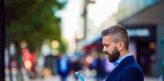 Hipster manager holding smartphone, texting outside in the street